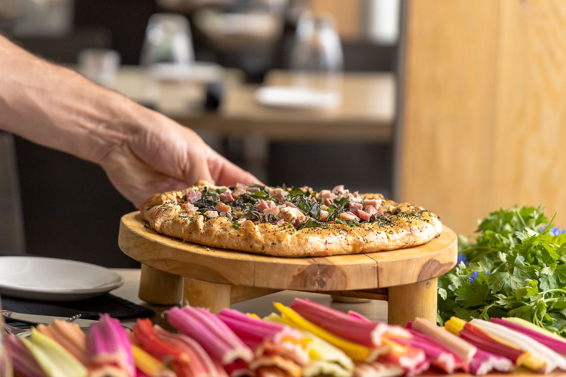Hand holding a freshly baked pizza with assorted vegetables at a restaurant.